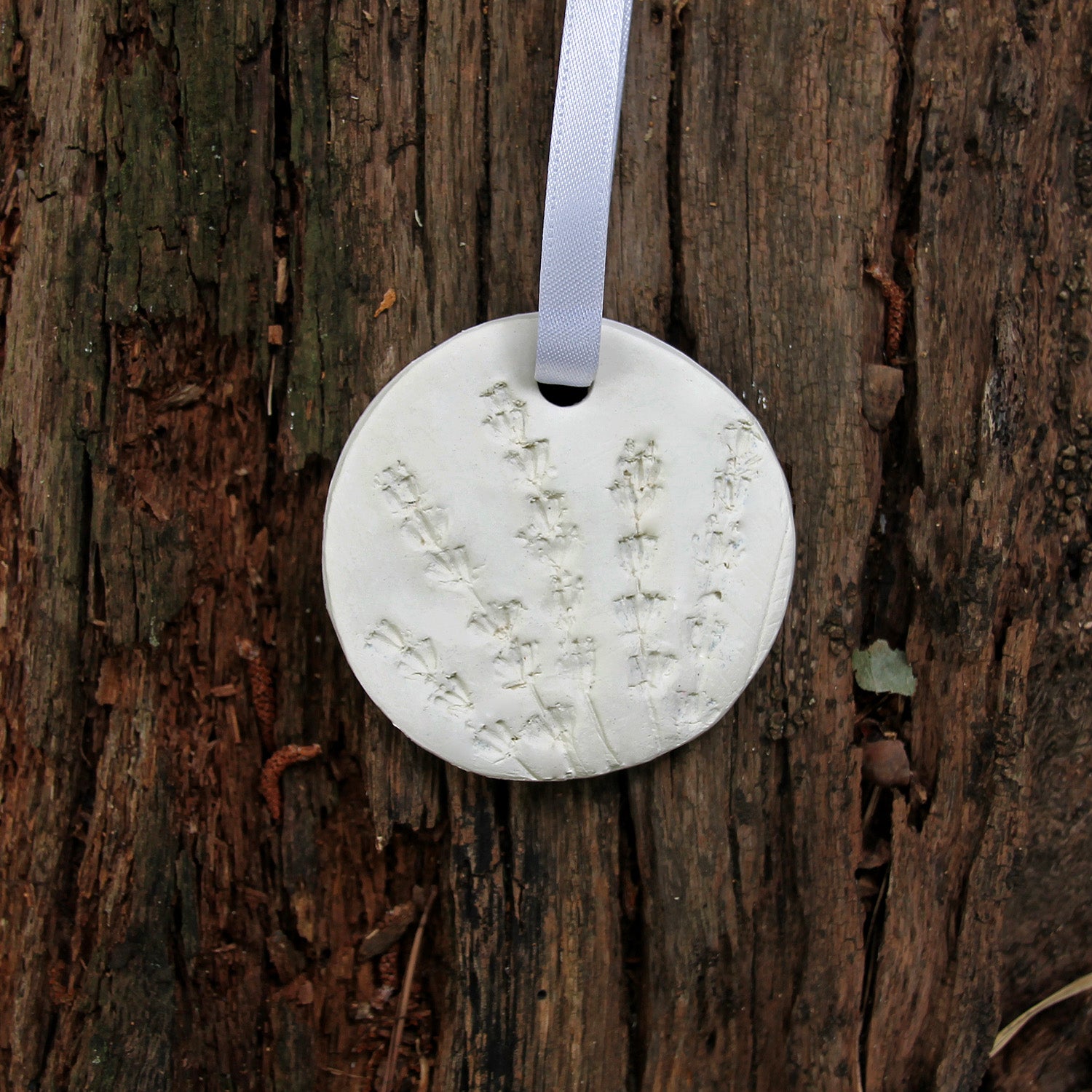 Round white clay diffuser with floral design hanging on a wooden surface