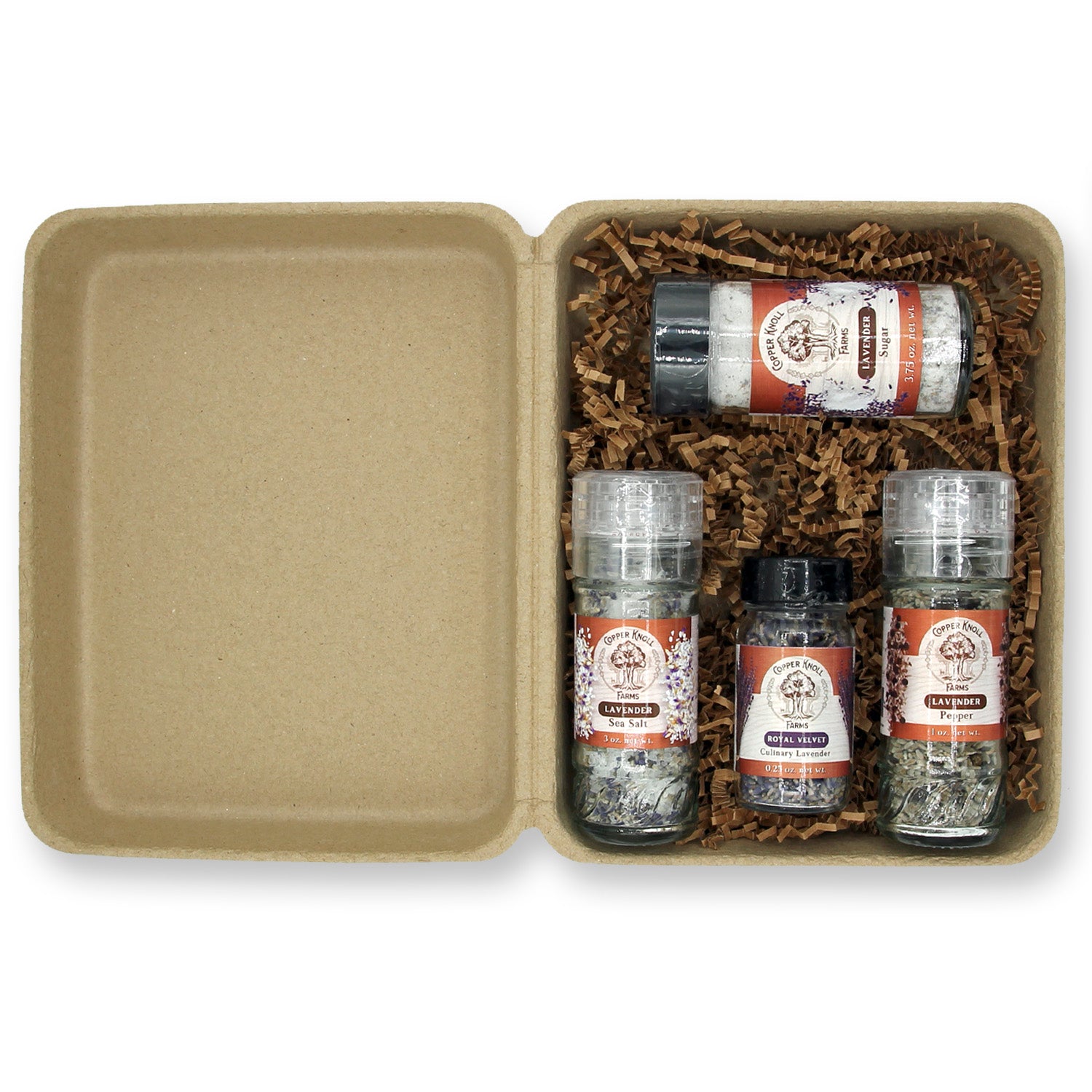 A gift box open to display three glass bottles filled with culinary lavender products, including sea salt, pepper, and sugar, packaged in biodegradable paper with a copper raffa tie.